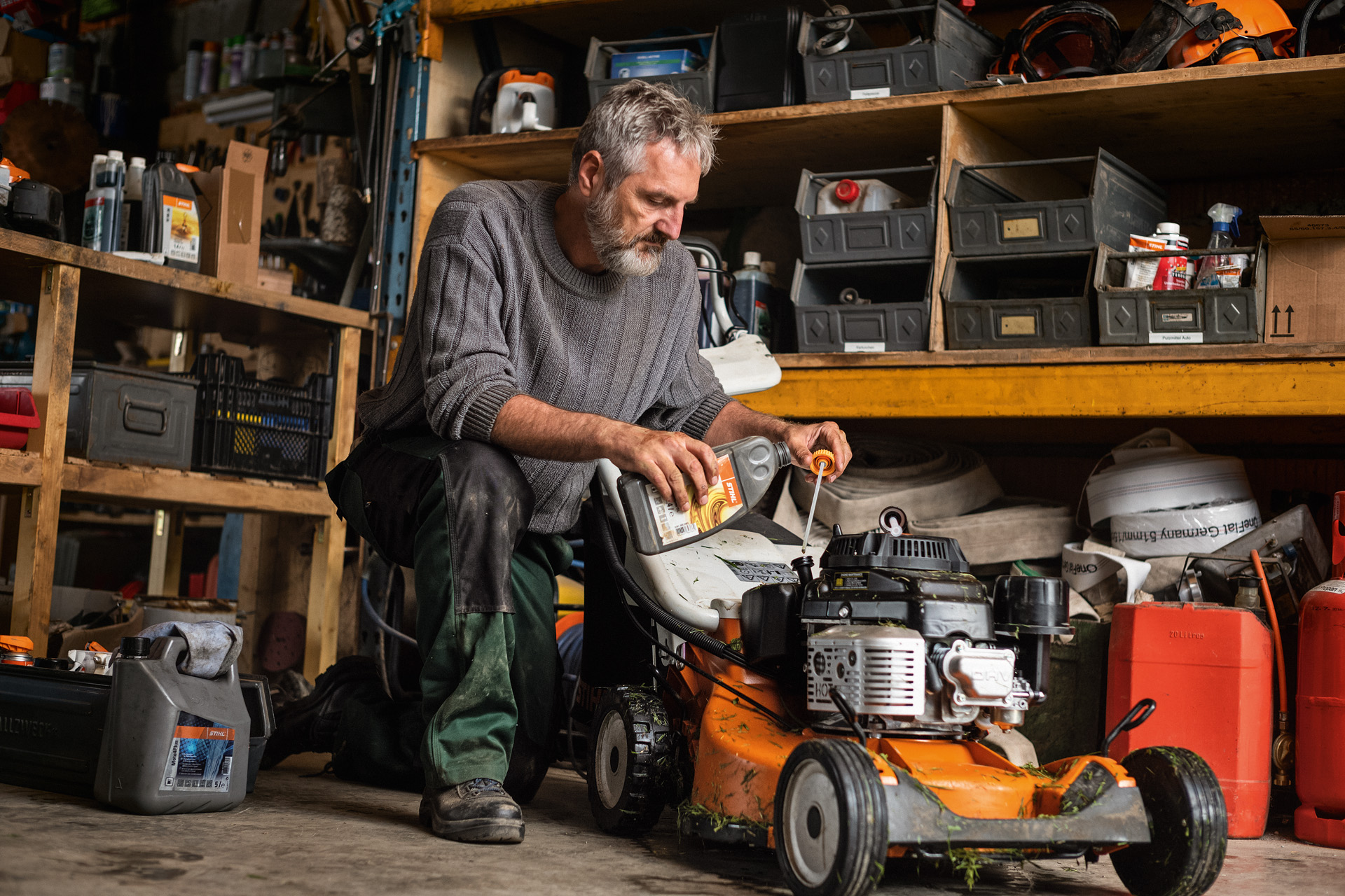 ガレージでガソリン芝刈り機STIHL RM 756をメンテナンスする男性