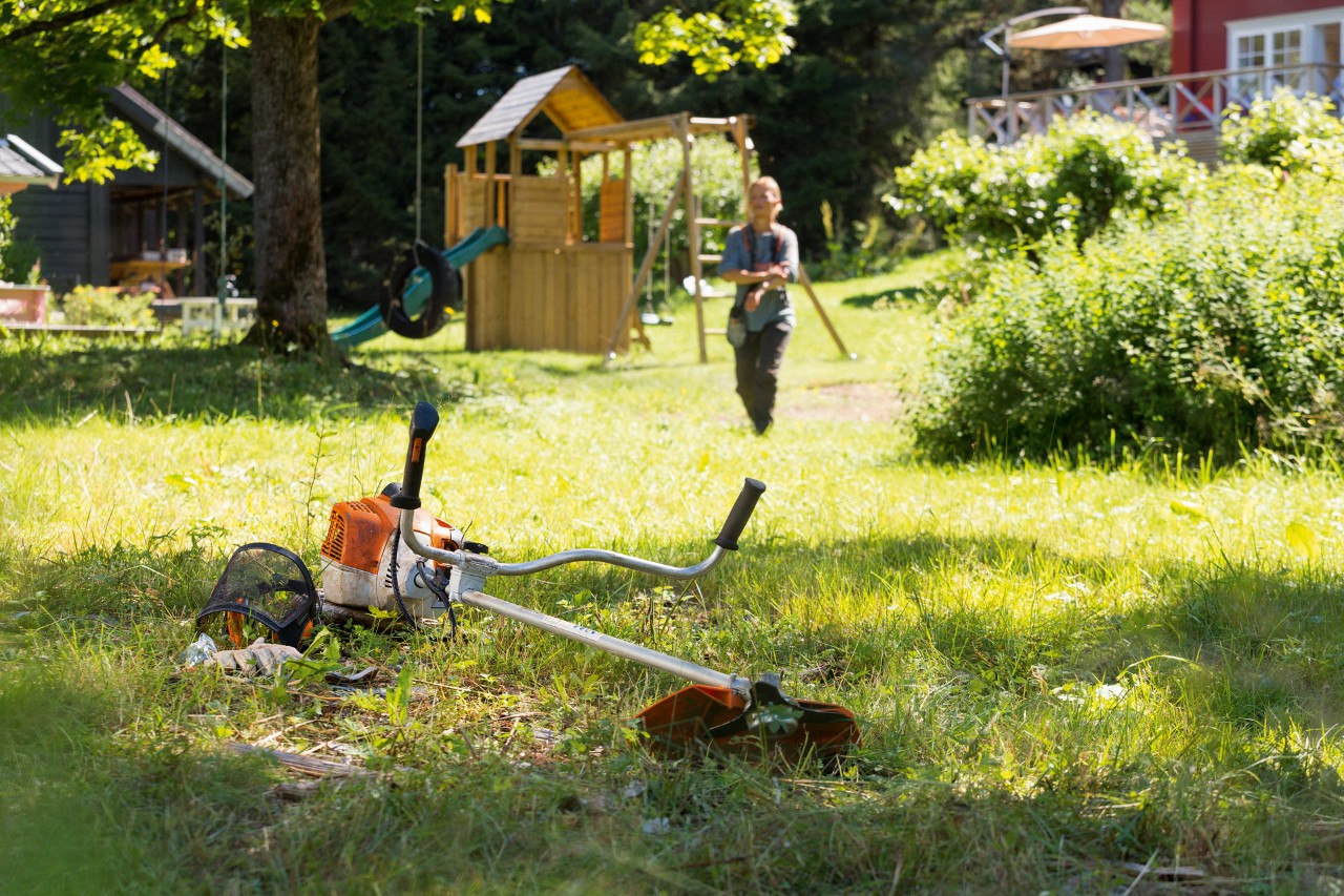 草の中に横たわっている刈払機STIHL FS 240、その背景でメンテナンスの準備をしている男性
