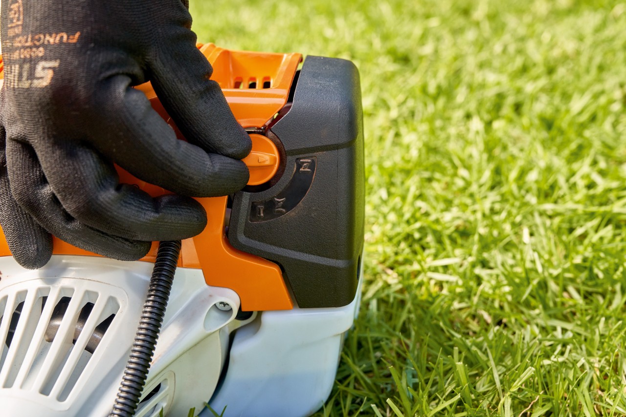エンジン刈払機STIHL FS 91の燃料ポンプのレバーを調整して、同機を始動しようとしている男性