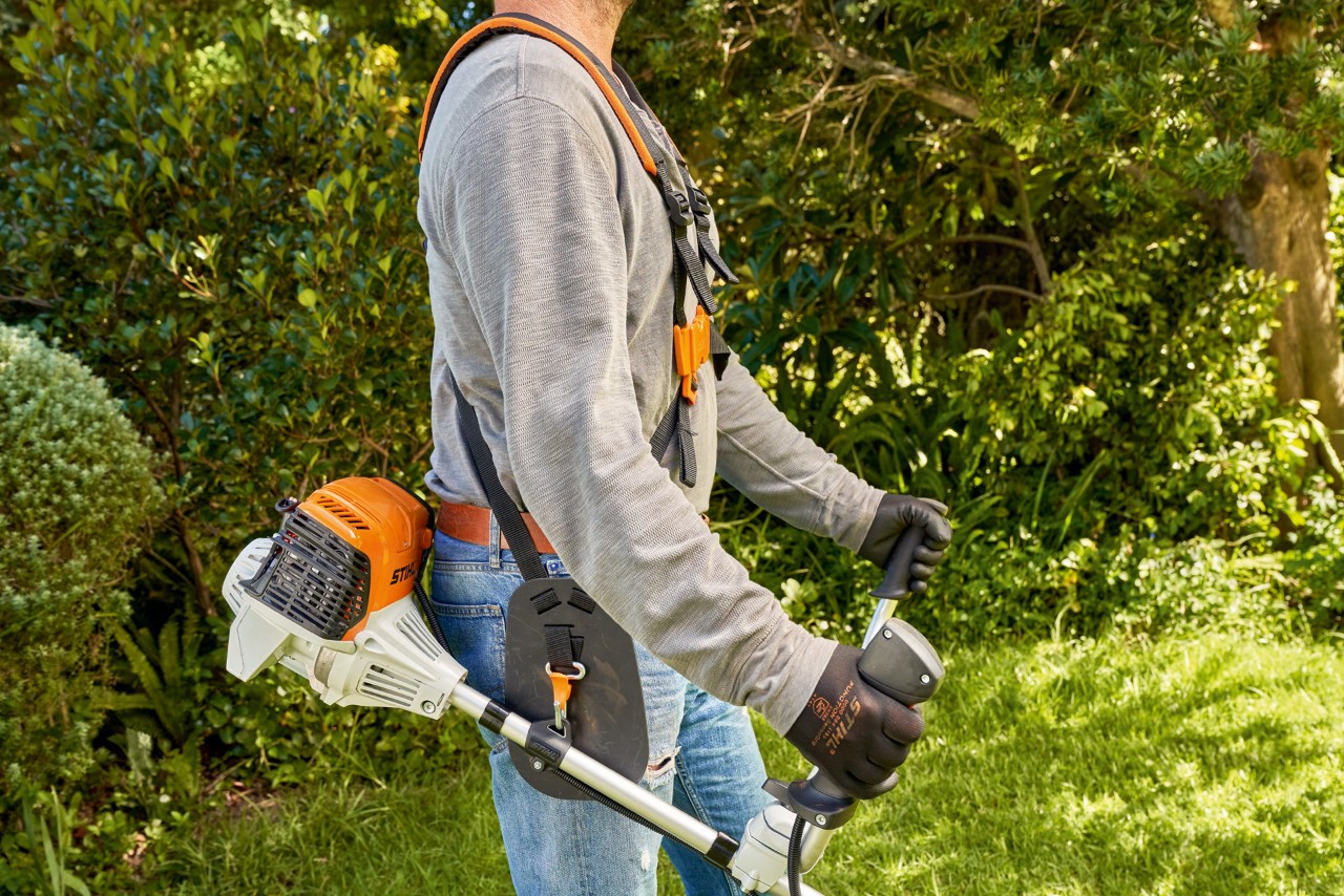 エンジン刈払機STIHL FS 91を地面から持ち上げて、同機で芝刈りを始めようとしている男性 