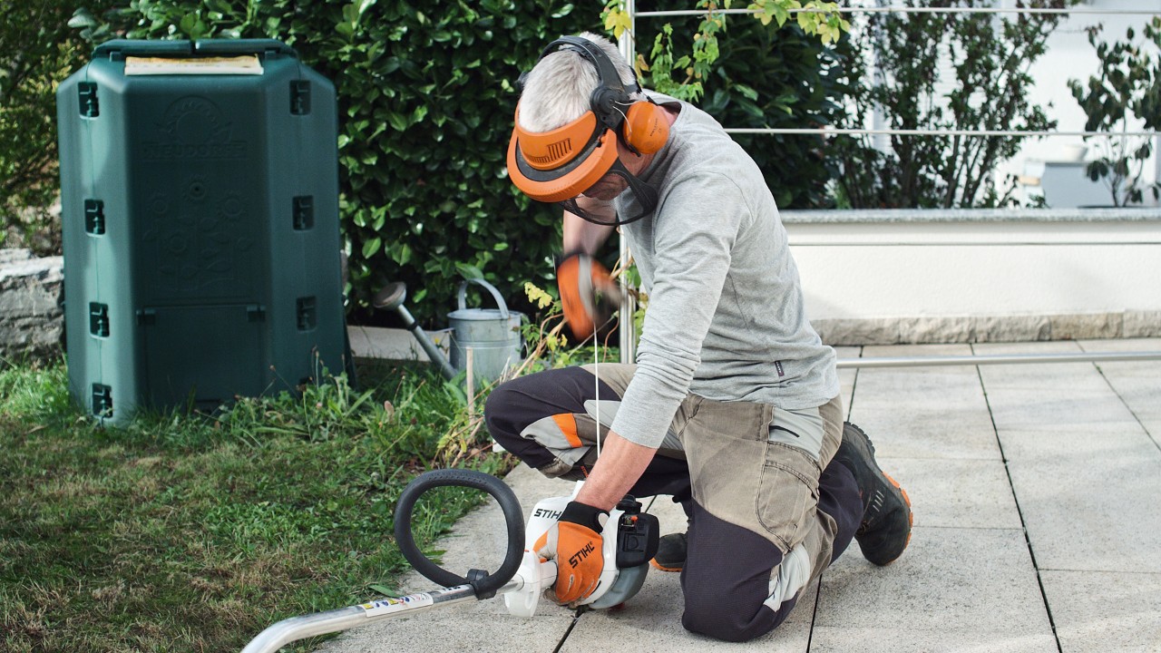 作業用防護服を着用して、エンジン刈払機STIHL FS 38のスターターロープを引っ張っている人物