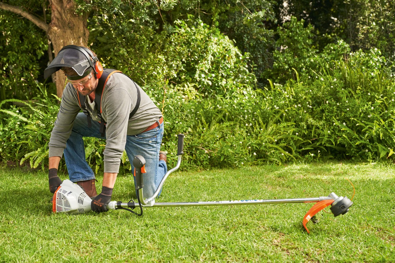 エンジン刈払機STIHL FS 56を地面にしっかりと押し付けて、同機を始動しようとしている男性