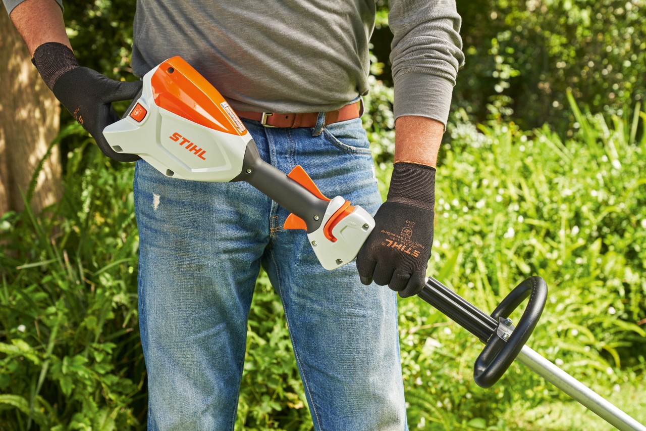 作業手袋を着用して、バッテリー刈払機STIHL FSA 60のバッテリーを点検して、刈払機を始動しようとしている男性