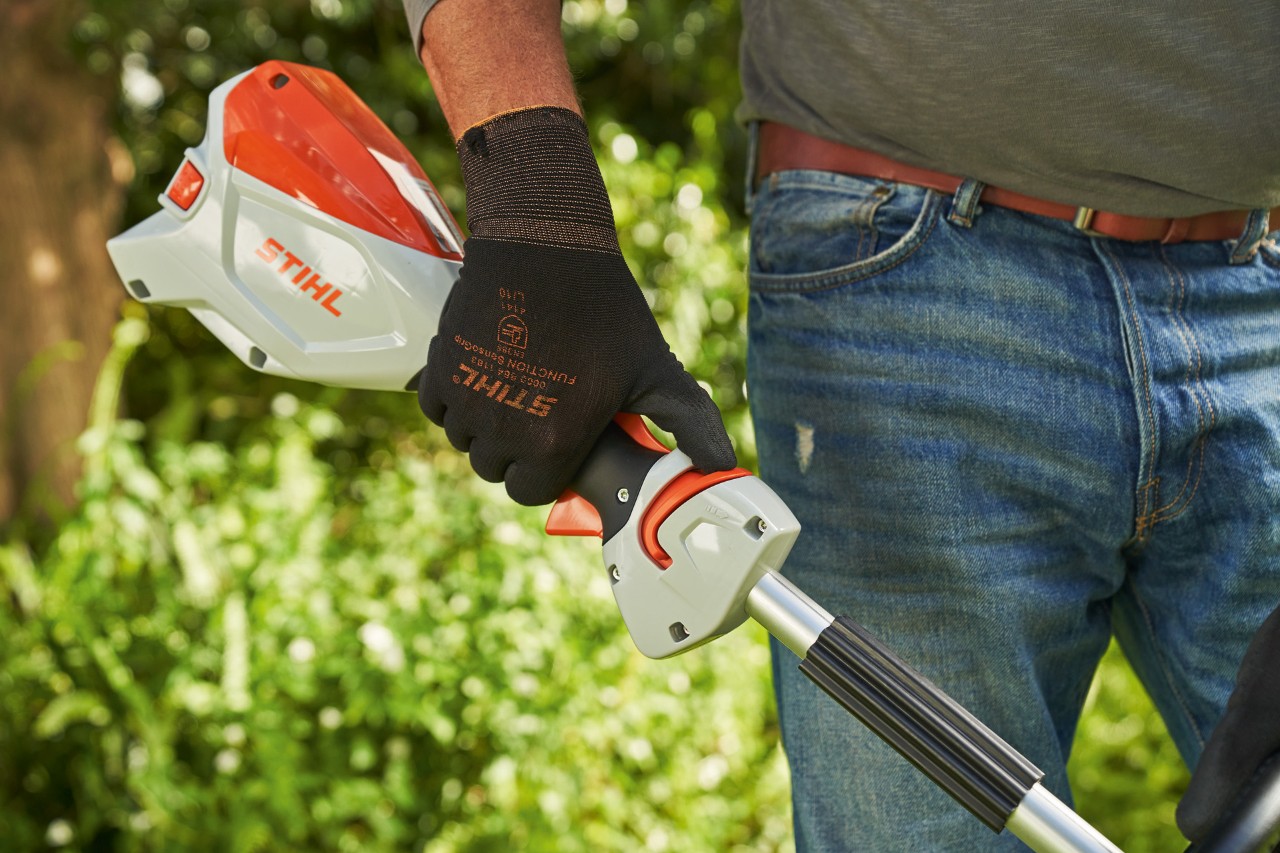 作業手袋を着用して、バッテリー刈払機STIHL FSA 60のリリーススライドをループハンドルの方向に押している男性