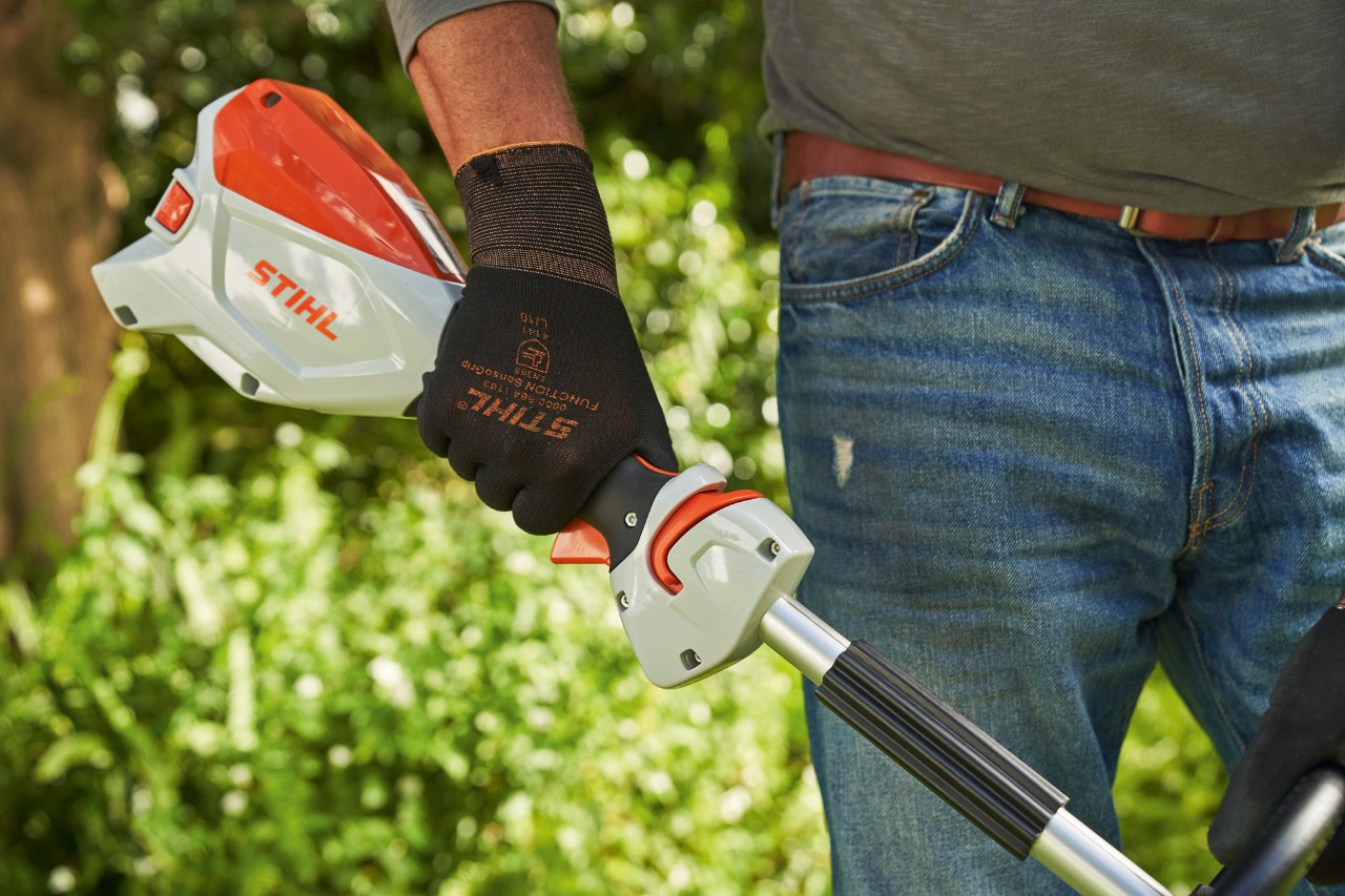 作業手袋を着用して、バッテリー刈払機STIHL FSA 60のトリガーロックアウトを押している男性 