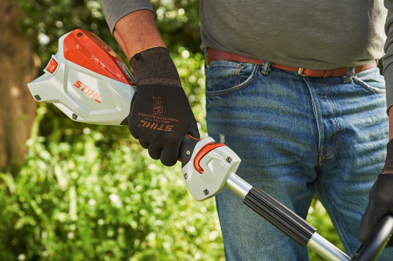 作業手袋を着用して、バッテリー刈払機STIHL FSA 60のトリガーを押して、同機を始動しようとしている男性
