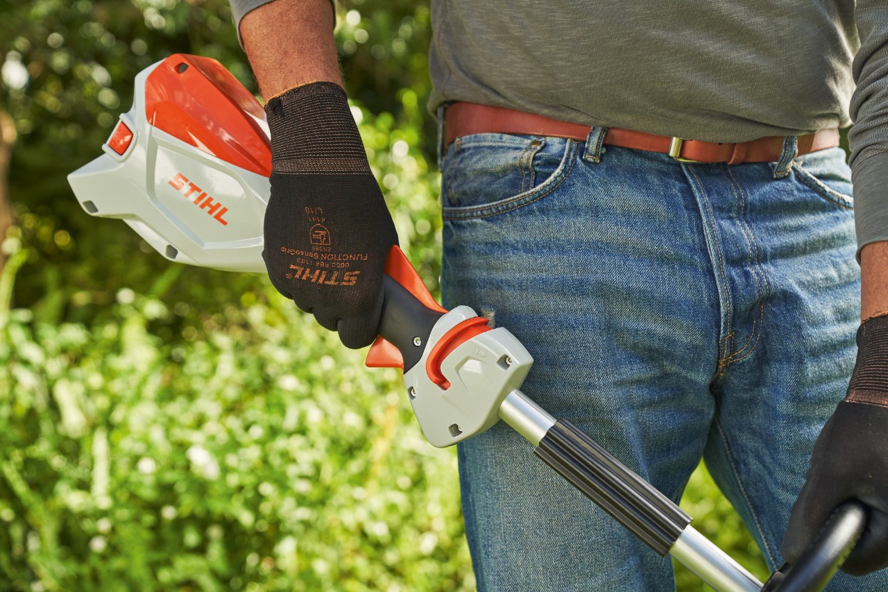 作業手袋を着用して、バッテリー刈払機STIHL FSA 60のトリガーを放して、同機をオフにしようとしている男性