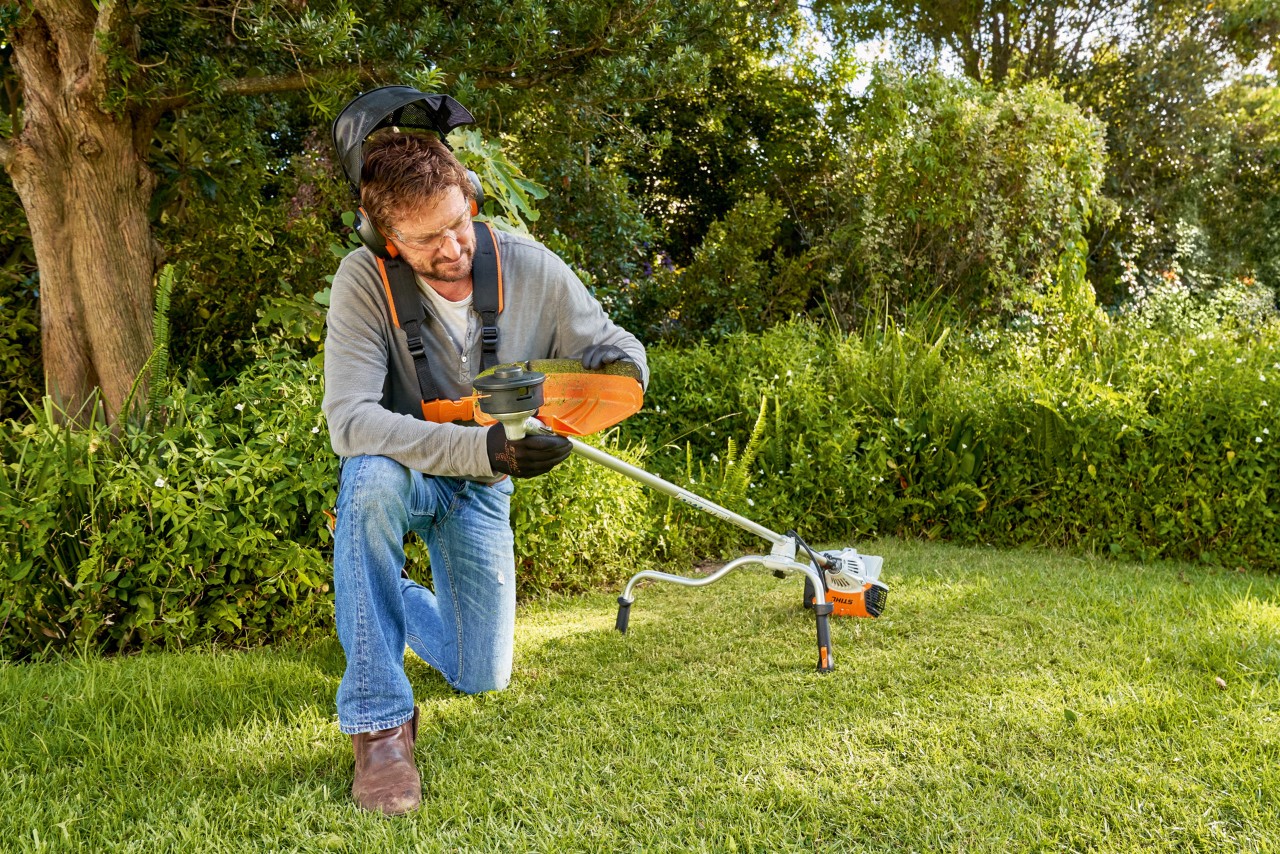庭で刈払機を準備して、カッティングアタッチメントを交換しようとしている男性