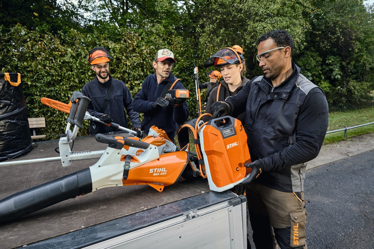 バッテリーブロワーSTIHL BGA 200や背負式バッテリーSTIHL AR 2000 LなどのSTIHL製品を積んだ車両の荷台に立つ、STIHLの作業用防護服を着た3人の男女 
