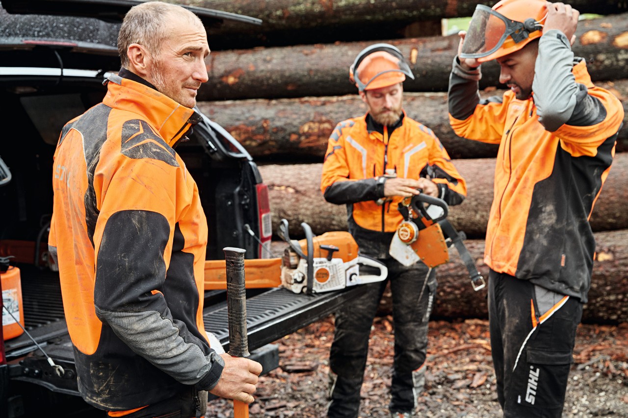 トランクの開いた車の横にいるSTIHLの作業用防護服を着用した3人の男性