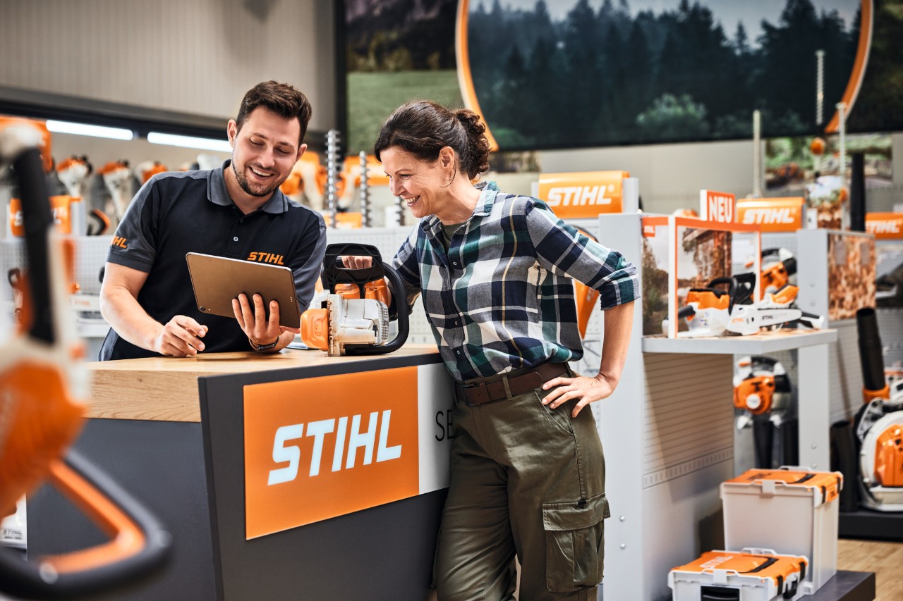 STIHLのヘッジトリマーを購入する若い女性にアドバイスするSTIHL販売店店員